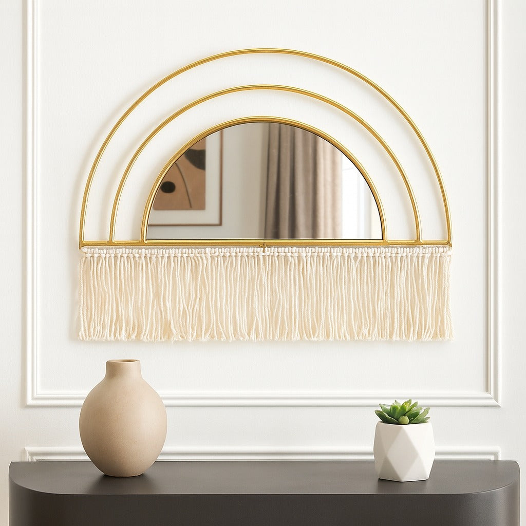 Decorative mirror with gold frame and fringe above a console table with a vase and plant.